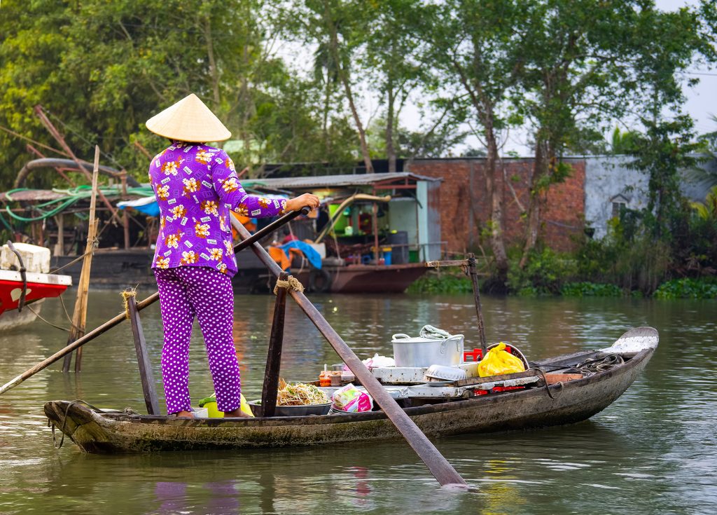 A vendor at Phong Dien floating market rowing her boat and facing away from the camera.