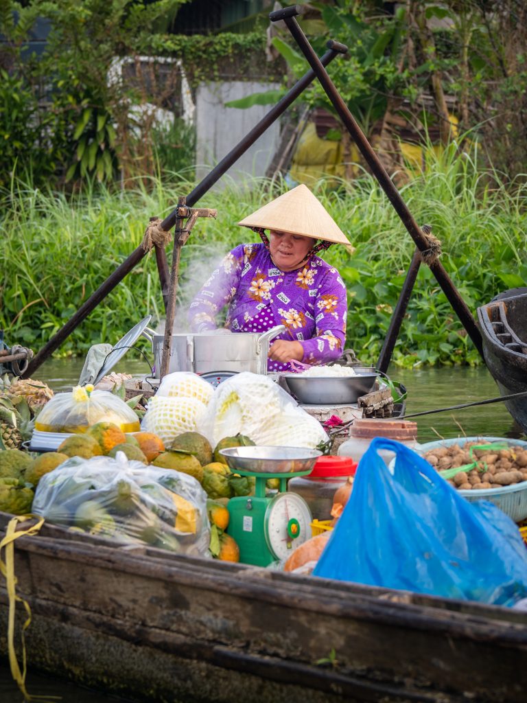 Image of a vendor at Phong Dien floating market making soup on her boat.